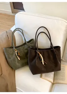 Dettaglio borsa tote in pelle scamosciata verde oliva con nappine di legno su divano