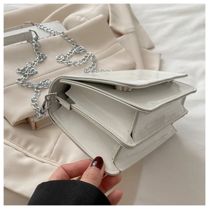 Detail of white patent leather crossbody bag showing multi-layered accordion design and chain