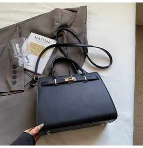 Close-up of black lychee grain leather tote featuring gold metal buckle and sturdy handles