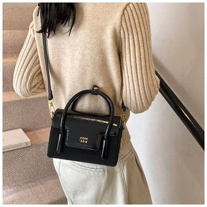 Detail of black glossy crossbody bag with gold hardware and logo on model's shoulder