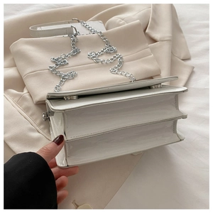 Detail view of white patent leather crossbody bag with multi-compartment accordion structure