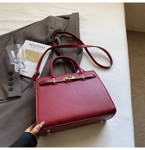 Detailed view of burgundy leather handbag with golden twist-lock and metal feet