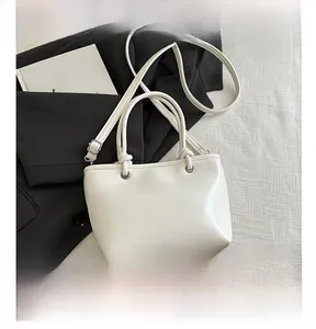 Détail d'un sac seau en cuir blanc avec doubles poignées et une longue bandoulière