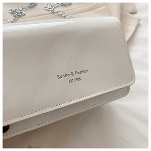 Close-up of white glossy crossbody bag with silver chain and modern lettering design