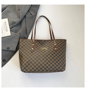 Detail of dark brown tote bag featuring M-pattern print and golden bow buckle