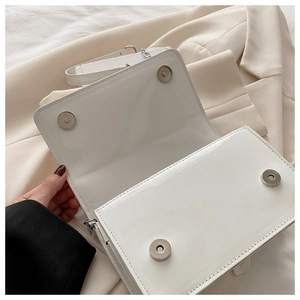 Detail of white patent leather bag with magnetic snap closure and silver chain strap