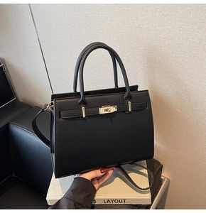 Detail of black cross-grain leather handbag with golden twist lock and adjustable strap