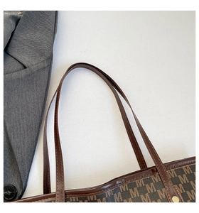 Close-up of M-letter print tote bag with brown leather handle and metal rivet details