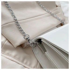 Close-up of white patent leather bag featuring silver metal chain and side gusset design