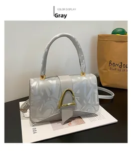 Détail du sac bandoulière gris avec boucles dorées et motif de lettres abstraites