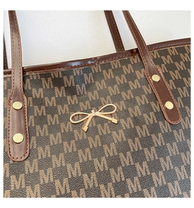 Detailed close-up of brown tote bag showing gold bow and monogram patterned texture