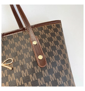 Detail of the brown tote bag featuring golden rivets and M-letter monogram pattern