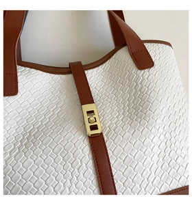 Detail of white textured leather tote bag featuring brown trim and gold metal twist lock