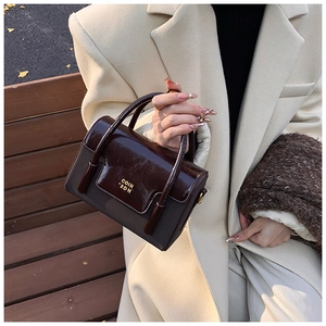 Detail of a dark brown crossbody bag featuring glossy leather and a gold metallic logo