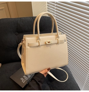 Detail of cream Kelly bag with litchi texture and gold hardware on a velvet chair