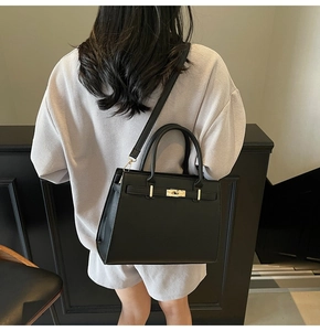 Detail of black leather satchel with golden clasp worn over the shoulder by a model