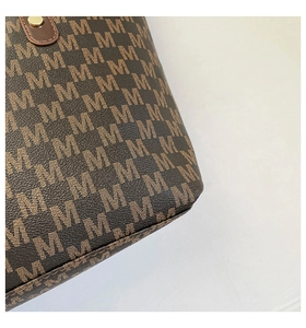 Detailed macro shot of brown textured tote bag with monogram pattern and golden metal stud