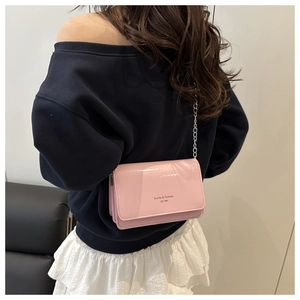 Detail of pink patent leather crossbody bag with silver chain and brand logo lettering
