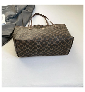 Macro view of brown monogram tote bag showing textured synthetic leather and sturdy handles
