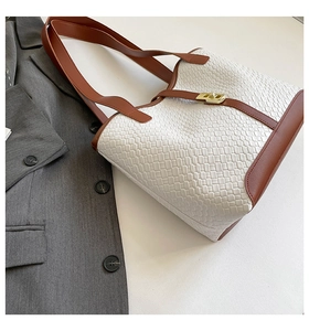 Detailed close-up of woven texture tote bag with brown leather trim and golden lock
