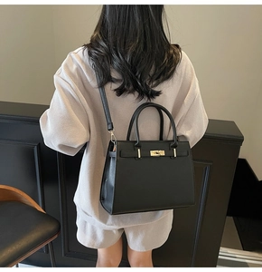 Detailed view of black minimalist Kelly handbag featuring elegant gold metal lock and leather strap