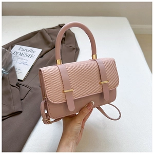 Pink textured crossbody bag with gold buckle and top handle in a minimalist setting