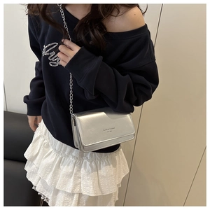 Detail of silver mirror crossbody bag with chain strap worn by model over white skirt