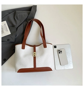 Detail of white textured tote bag with brown leather straps and gold buckle closure