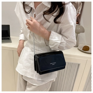 Detail of glossy black patent leather crossbody bag with silver chain strap and logo