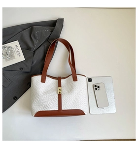 Close-up of white woven tote bag with brown handles and elegant gold metal clasp detail