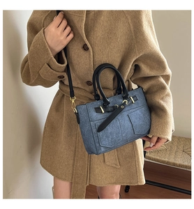 Detail of a denim-textured crossbody bag with decorative buckles on a wool coat