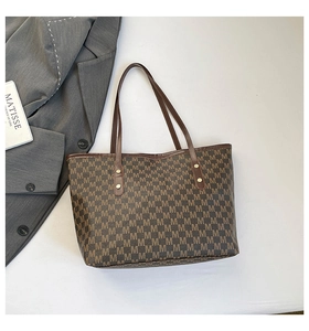 Detail of dark brown tote bag with repeating M pattern and leather handles on white background