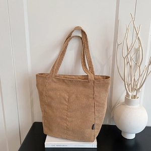 Brown corduroy tote bag with front pocket displayed on a book in a minimalist interior