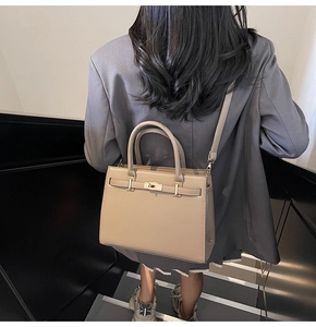 Detail of a khaki leather tote bag with gold metal lock buckle on a grey suit model