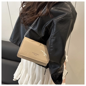 Detail of beige patent leather crossbody bag with silver chain strap and logo lettering