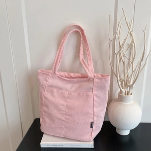 Pink corduroy tote bag for women with front pocket and fashion label on a white table