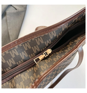 Macro shot of dark brown tote bag showing smooth metal zipper and monogram pattern