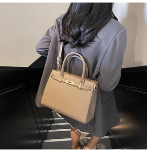 Detail of a khaki trapezoid satchel with metal twist lock shown on a model