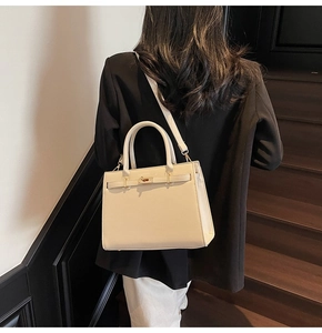 Detail shot of a cream leather trapezoid handbag with gold buckle on a model shoulder