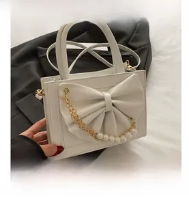 Détail d'un sac carré blanc avec grand nœud en cuir, chaîne perles et métal doré