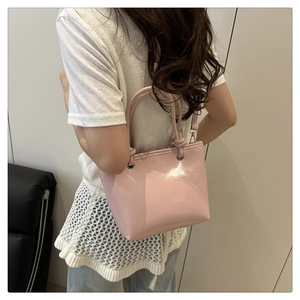 Pink patent leather bucket bag with twisted handle shown being carried by a model