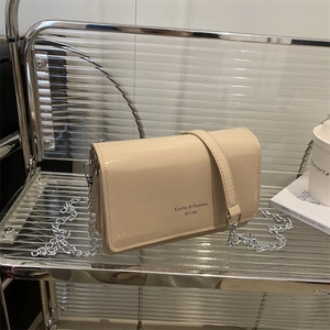 Beige patent leather crossbody bag with silver chain on a modern textured seat