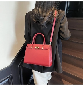 Model wearing red leather tote bag with gold lock buckle and black blazer