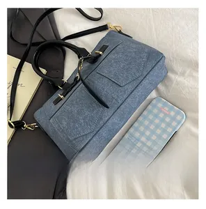 Close-up of blue denim rectangular handbag with black handles and gold hardware details