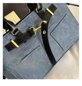 Close-up of stitching and gold hardware on blue denim handbag with black leather accents
