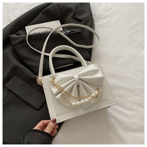 Détail d'un sac blanc à nœud papillon et chaîne en perles sur un blazer noir chic