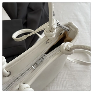 Detail der weißen Ledertasche mit Metallreißverschluss und Knotendetail am Schultergurt