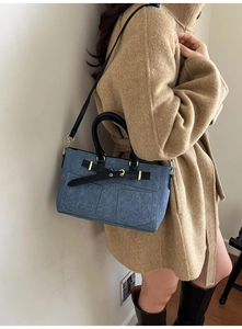 Blue denim tote bag with black handles styled on a wool coat for a casual winter look