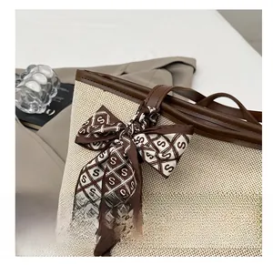Detail of woven tote bag with brown leather trim and decorative silk scarf accent