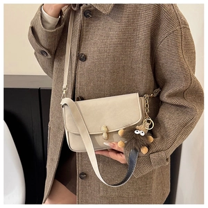 Detail of cream leather shoulder bag with gold peanut buckle and plush monster charm